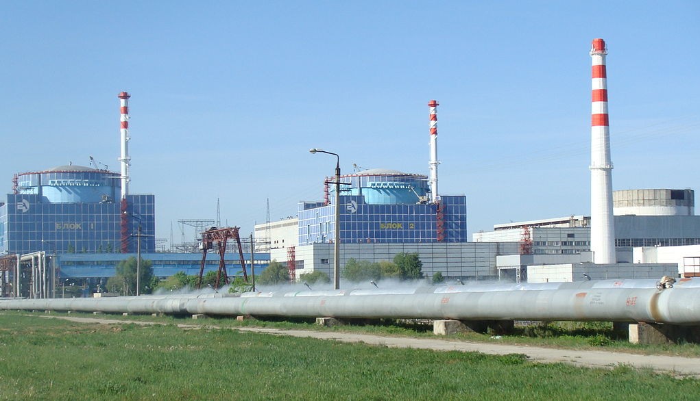 Pipelines running across foreground and power plant building with three stacks in backgrond