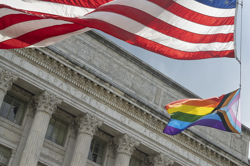 Pride Progress flag flying beneath the American flag