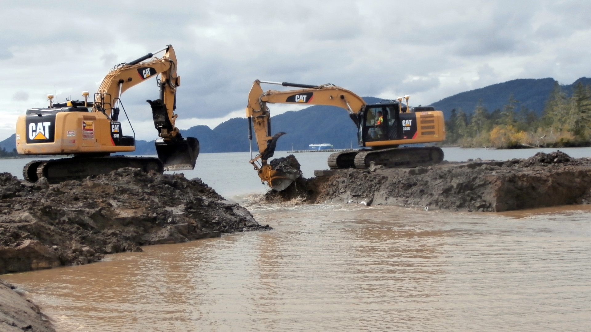 Water flows through a gap in a levee as construction equipment continues removal efforts.