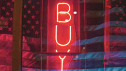 American flags on either side of a neon "buy" sign.