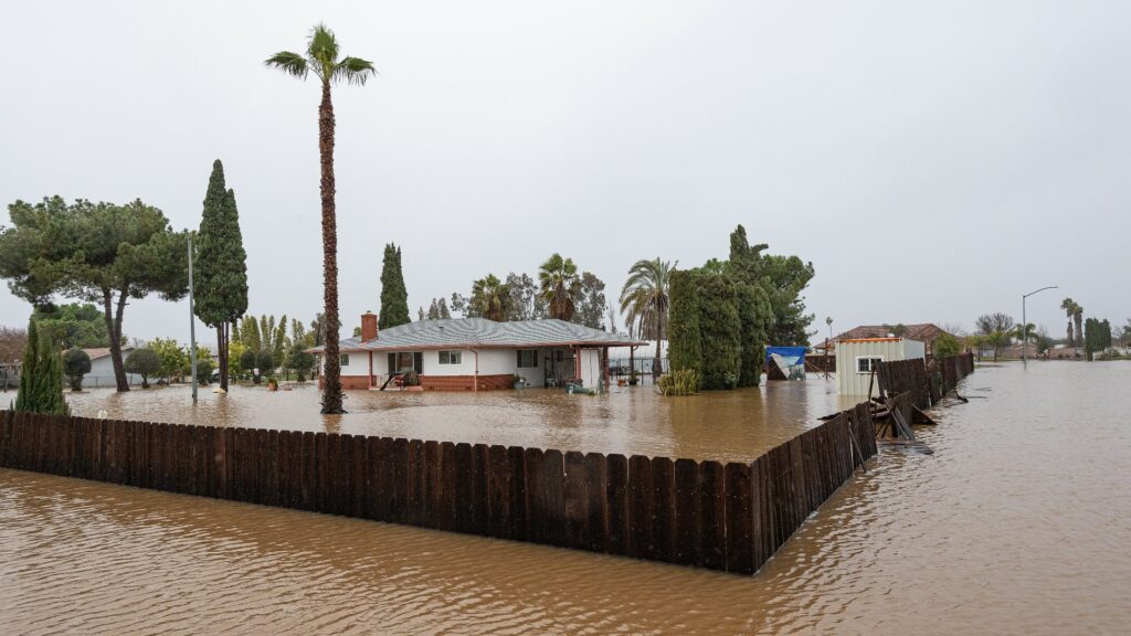House and fence with yard and street submerged in flood waters.