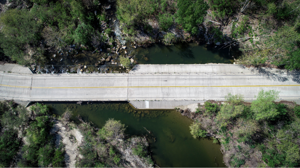 Aerial view of roadway bridge over river with trees on the banks.