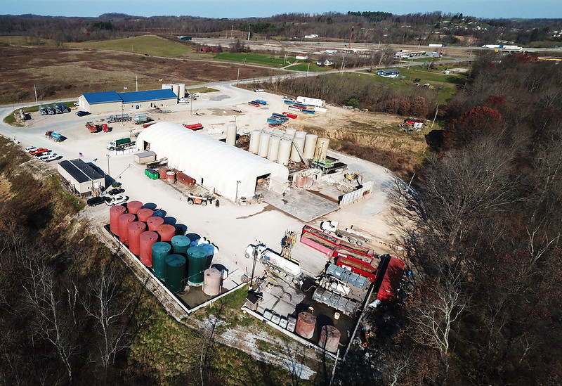 Aerial view of large lot with tanks and buildings surrounded by forest.