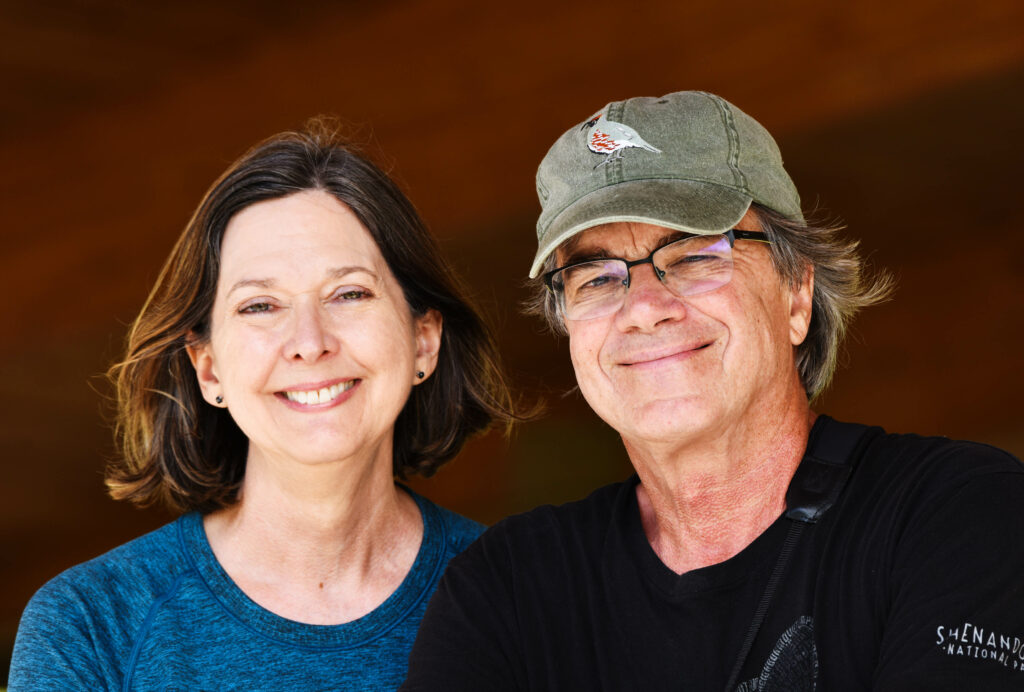 Head shot of white woman with brown hair and blue shirt and white man with black shirt and tan hat and glasses.