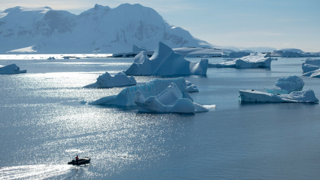 Small boat traveling through water with icebergs and Antarctic peninsula in the background