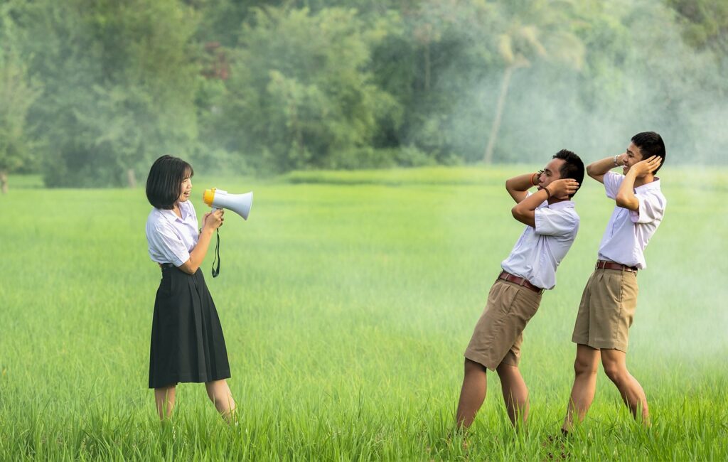 A woman makes an announcement through a bullhorn while two students recoil from the noise