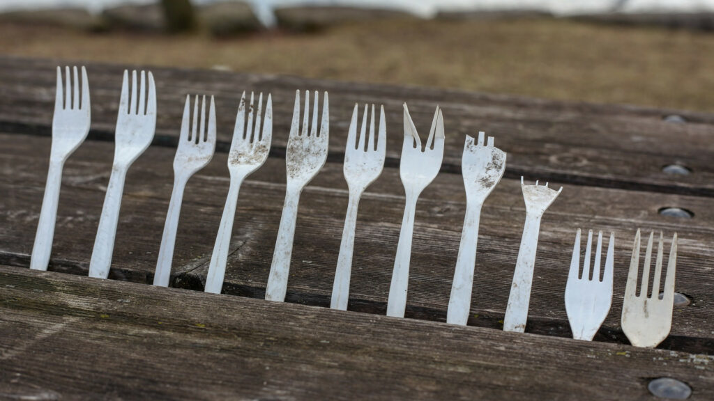 Dirty, broken plastic forks stick up between the boards of a picnic table