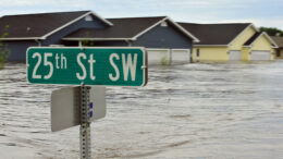 A street sign poking out of the water. Flooded homes in the background.