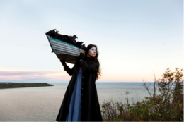 Meryl McMaster poses in a self portrait in a vast landscape.