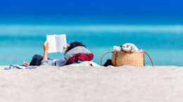 A woman lying on a beach with a book above her head