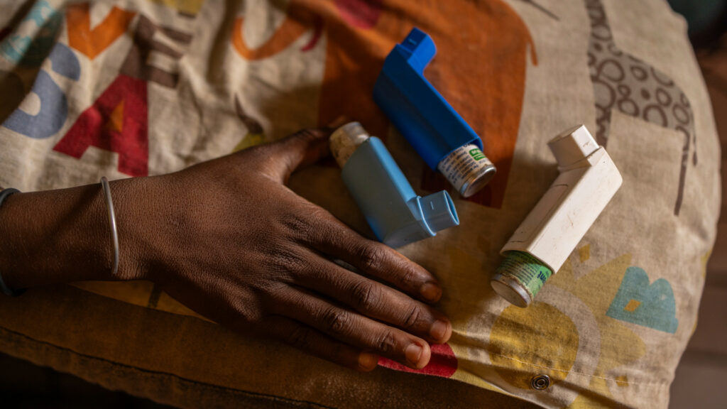 A Black woman's hand next to several asthma inhalers, with a colorful blanket underneath