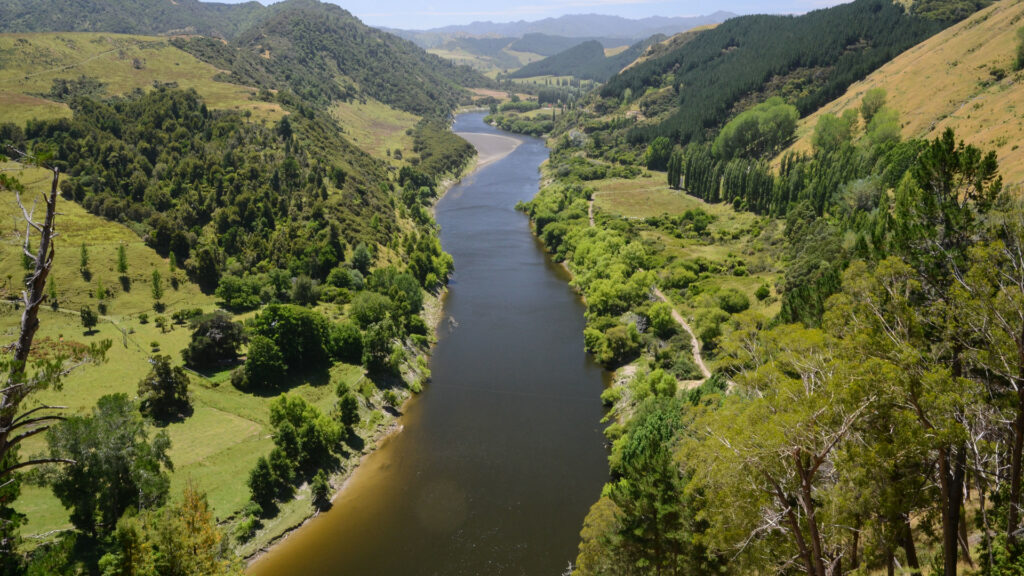 A powerful river runs down the center of the image, bracketed by hills and greenery