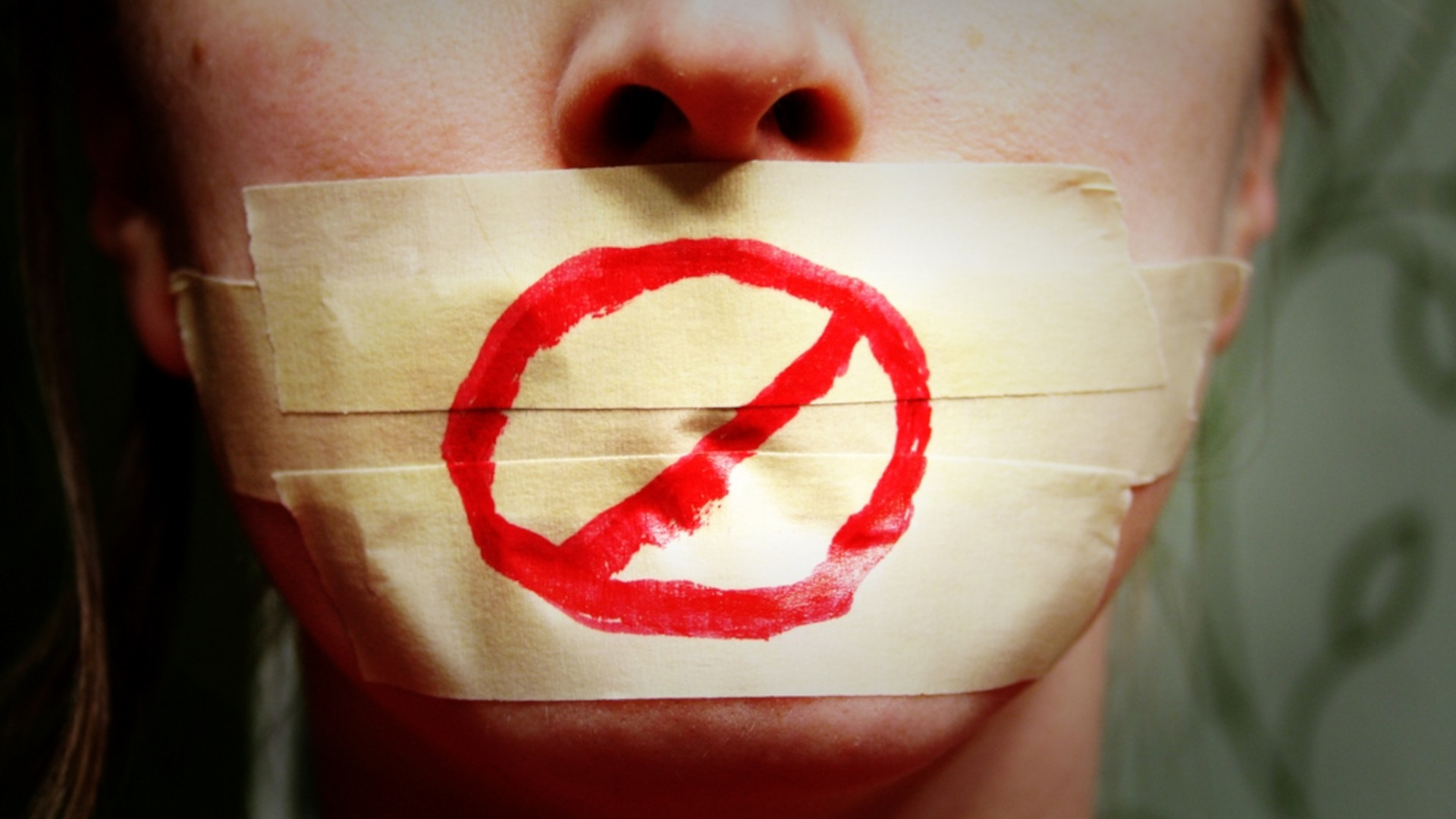 A woman with tape over her mouth and the "prohibited" symbol painted over it.