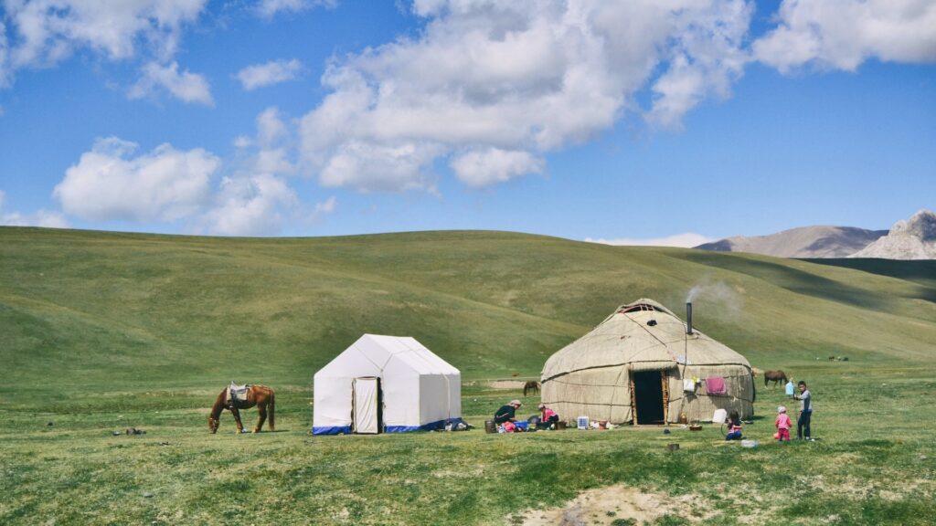 A horse grazes near a family, a yurt and a tent against the Kyrgyz mountains.