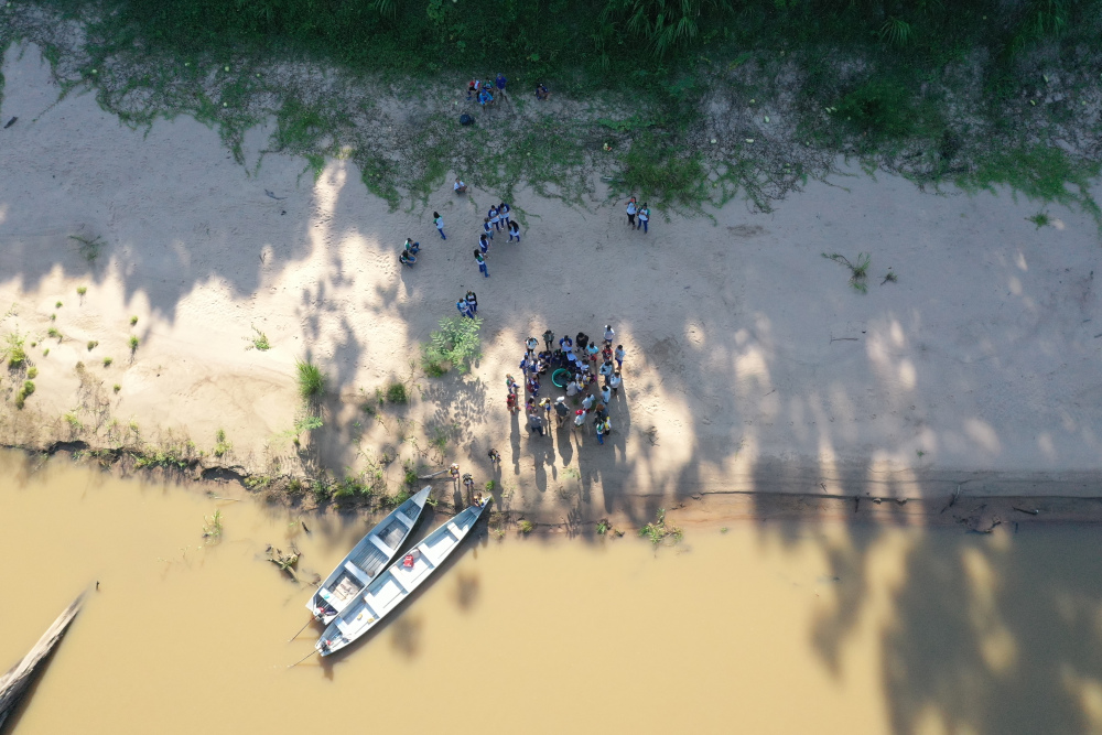 An aerial shot, river on the bottom, with people nearby two boats