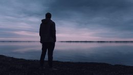 A lone man stares over the water at twilight