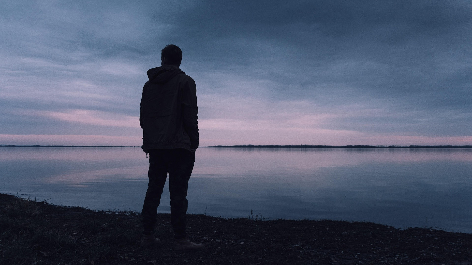 A lone man stares over the water at twilight