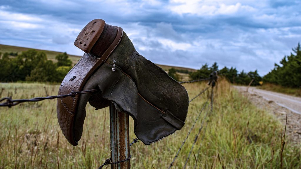A cowboy boot hangs on a barbed wire fence